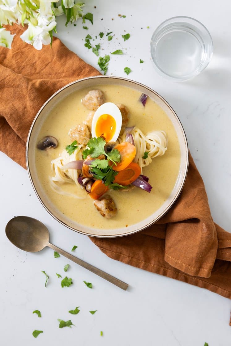 Asiatisk suppe med spicy kyllingboller og nudler servert med smilende egg, sopp og koriander