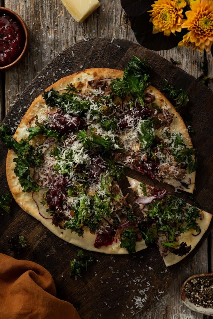 Hvit pizza med villhjortskav, sopp og sprø grønnkål, toppet med rørte tyttebær og lagret ost